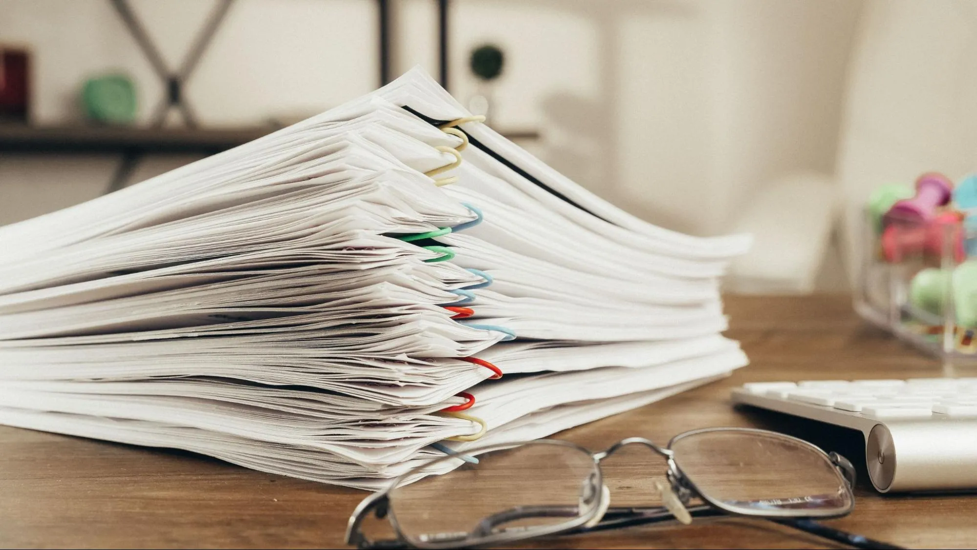 A stack of paper documents held together with clips beside a pair of glasses, representing the filings behind an intra-community registration