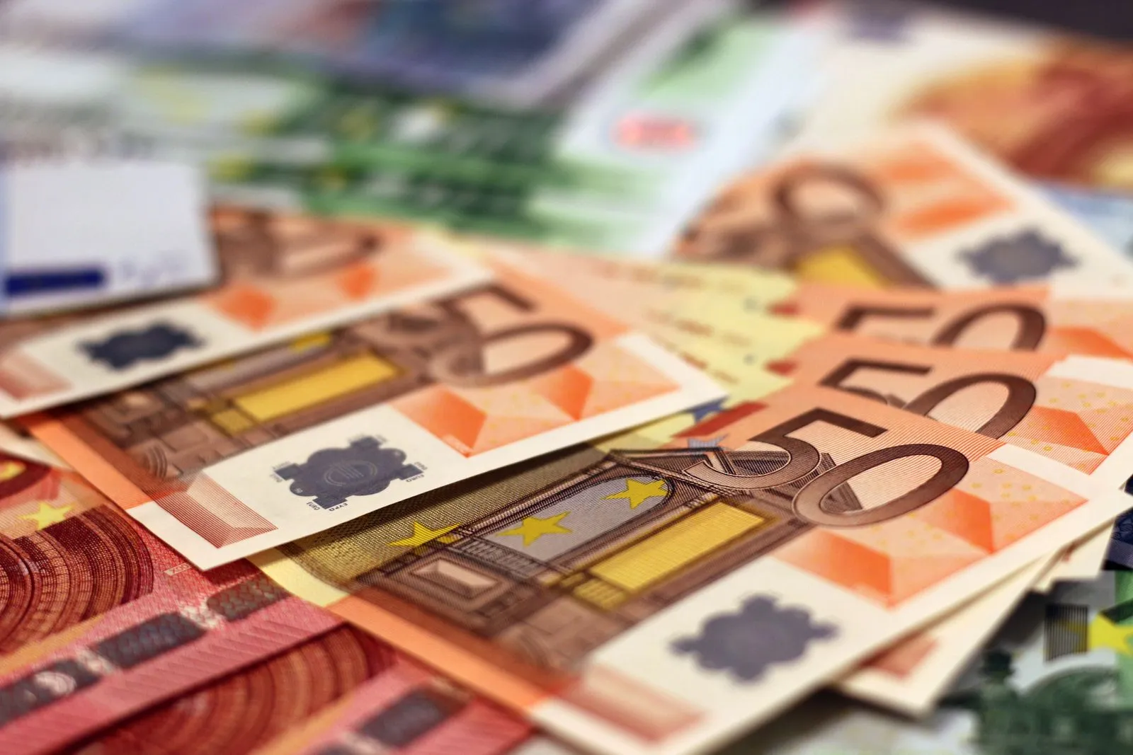 Close-up of fanned-out euro banknotes, mostly orange €50 notes, with €10 and €100 notes around them