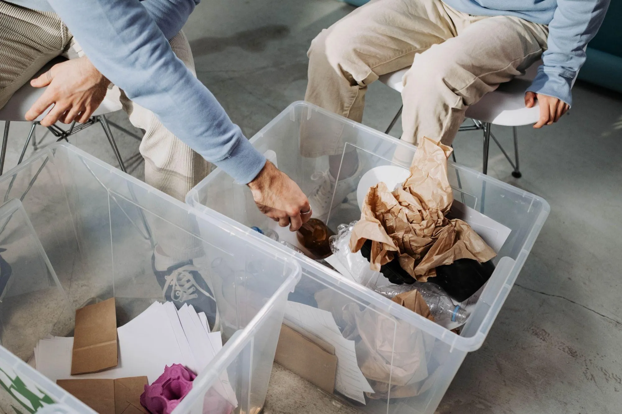 Two people sorting packaging waste — paper, plastic film and cardboard — into clear plastic storage boxes