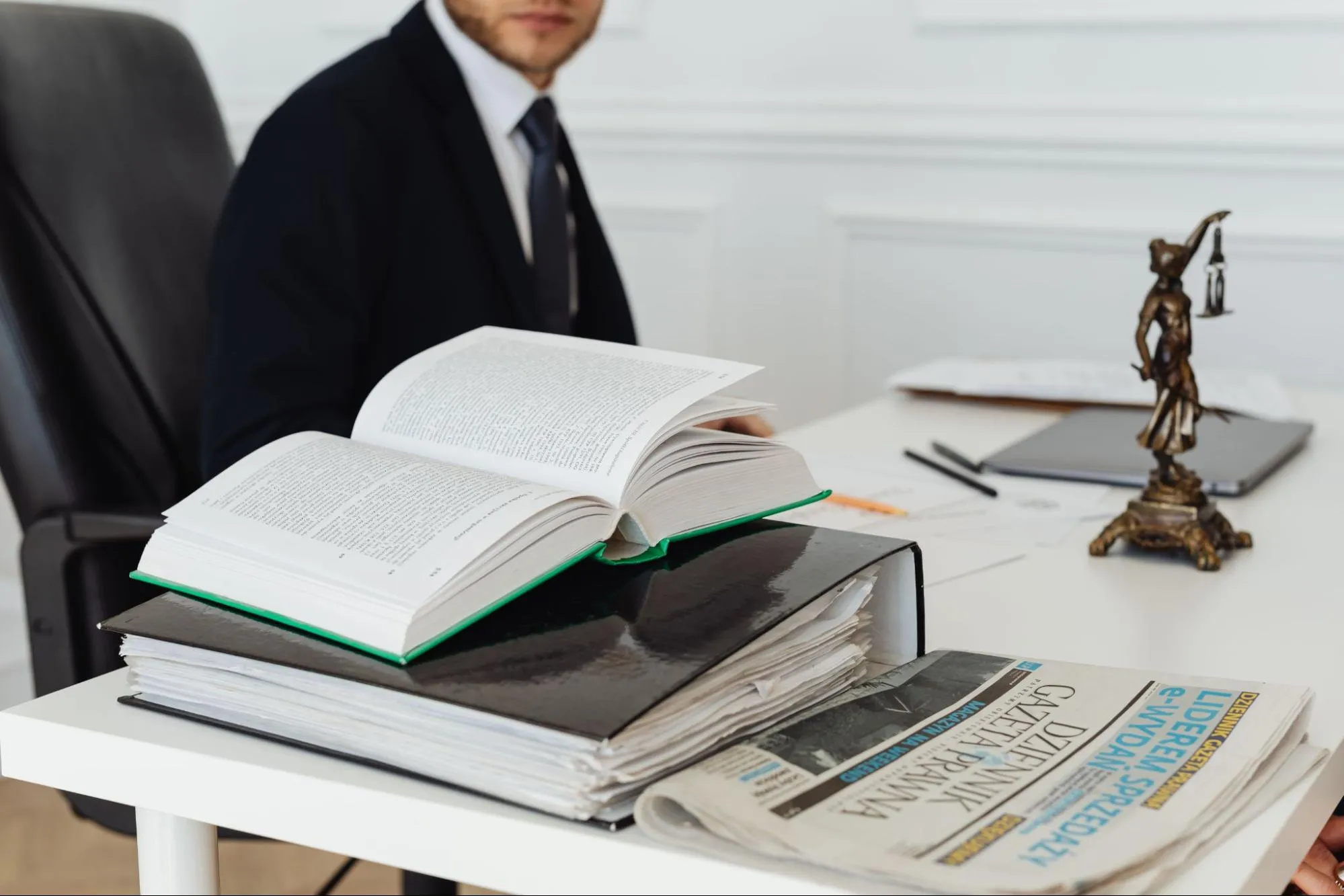 An open law book and a folded legal newspaper on a desk in front of a professional in a suit, representing the 2024–2025 reform of fiscal representation
