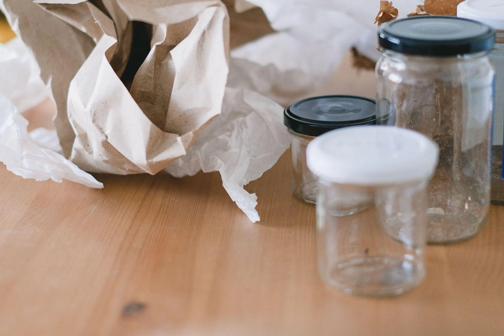 Crumpled kraft paper and tissue packaging beside empty glass jars on a wooden table