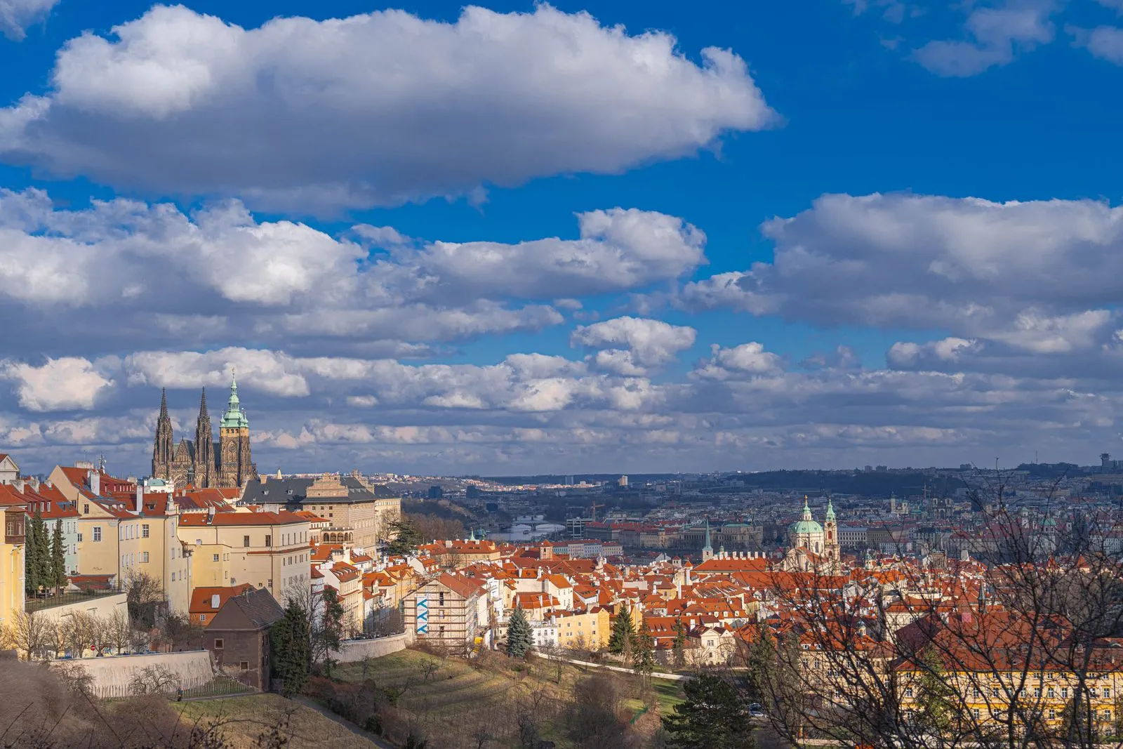 Panorama of Prague under a blue sky with large clouds, with St. Vitus Cathedral and the red roofs of the Lesser Town
