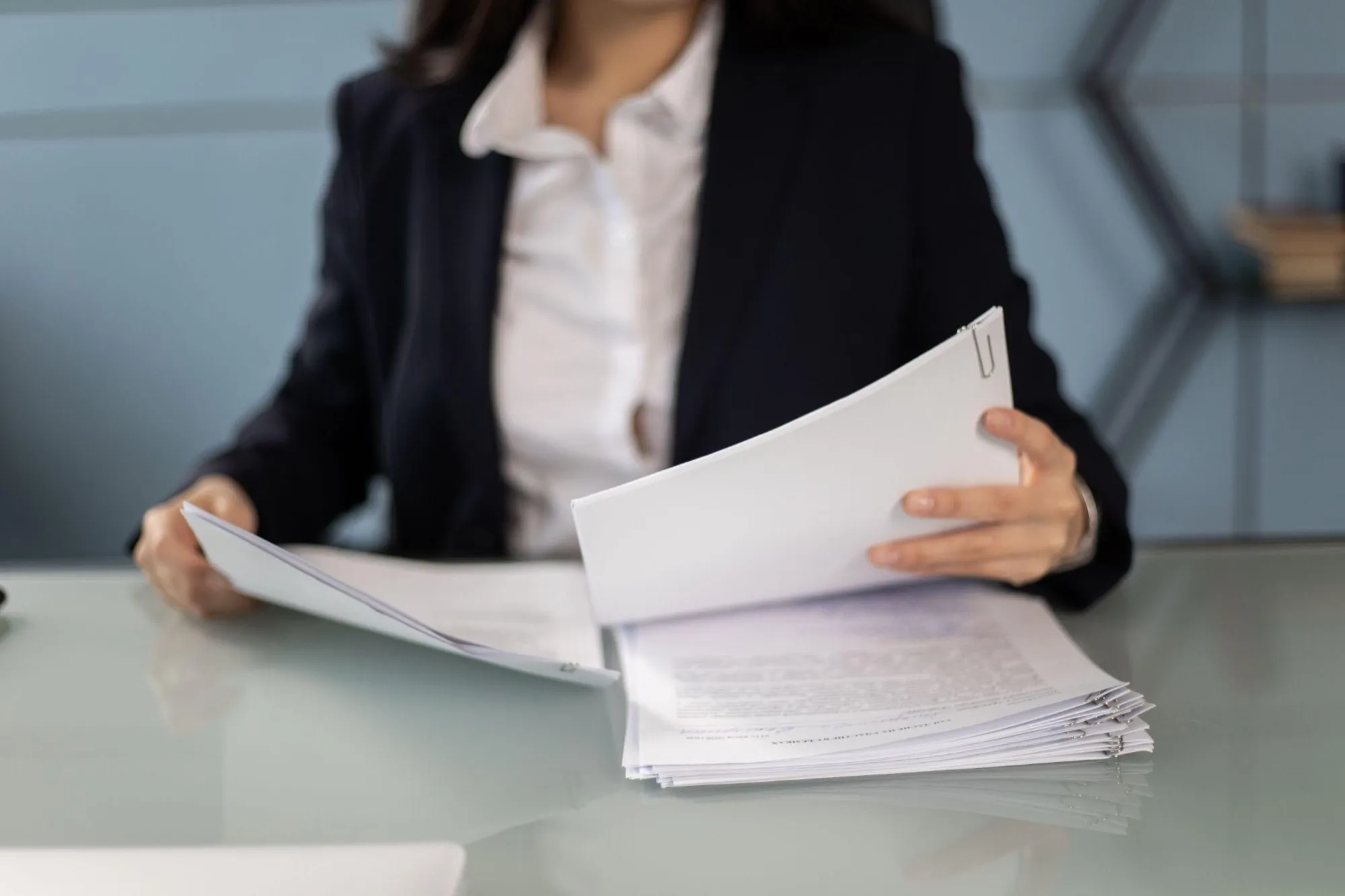 A person at a desk leafing through a thick stack of printed documents