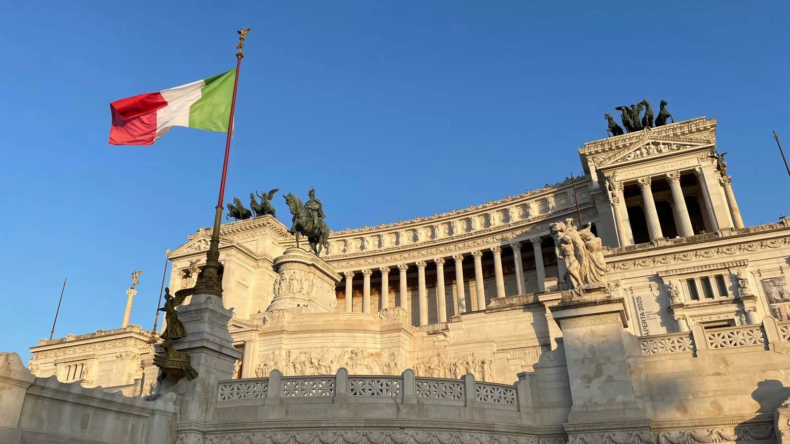 Italian flag flying in front of the Vittoriano monument in Rome under a clear blue sky