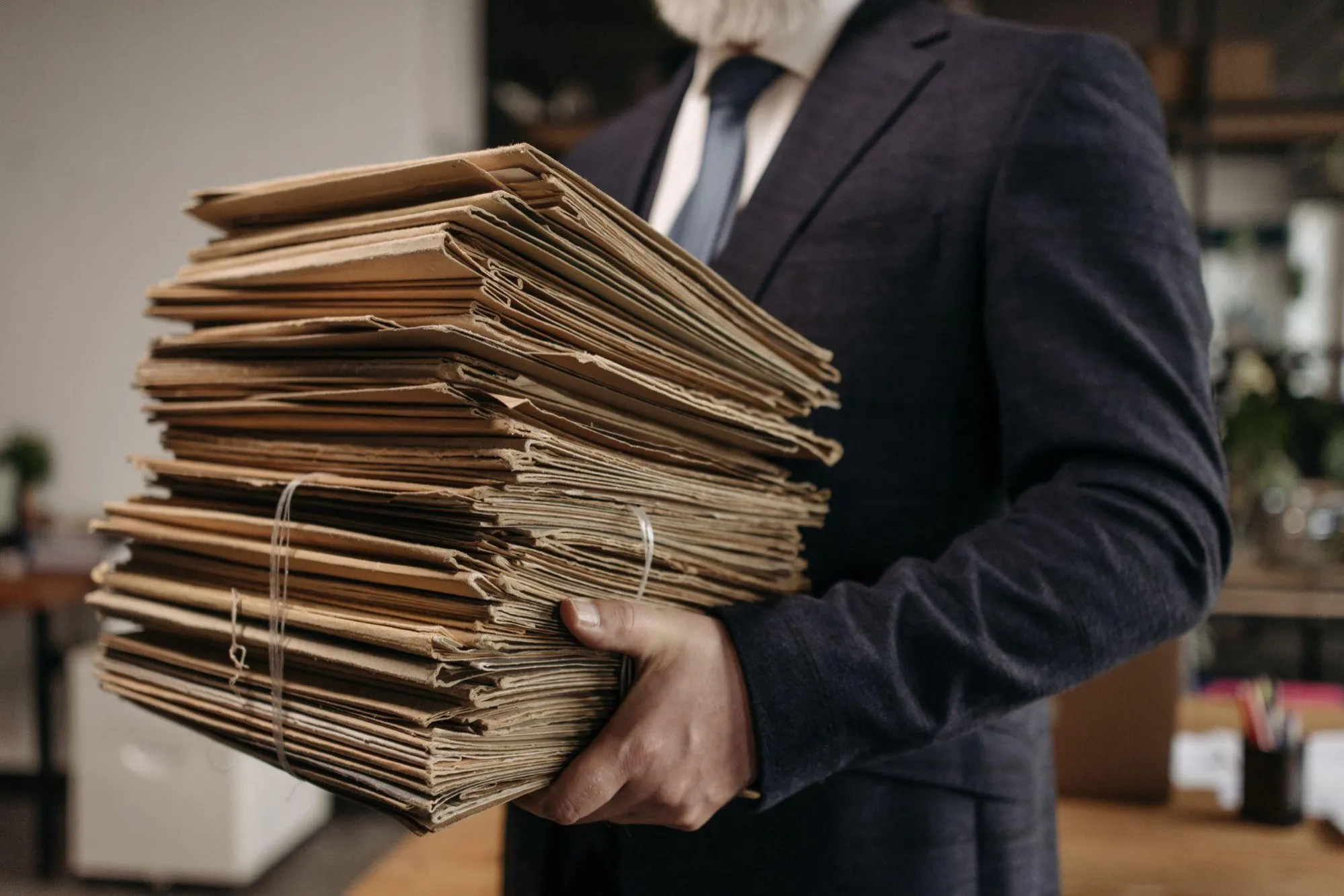 A person in a suit carrying a tall stack of tied paper document folders